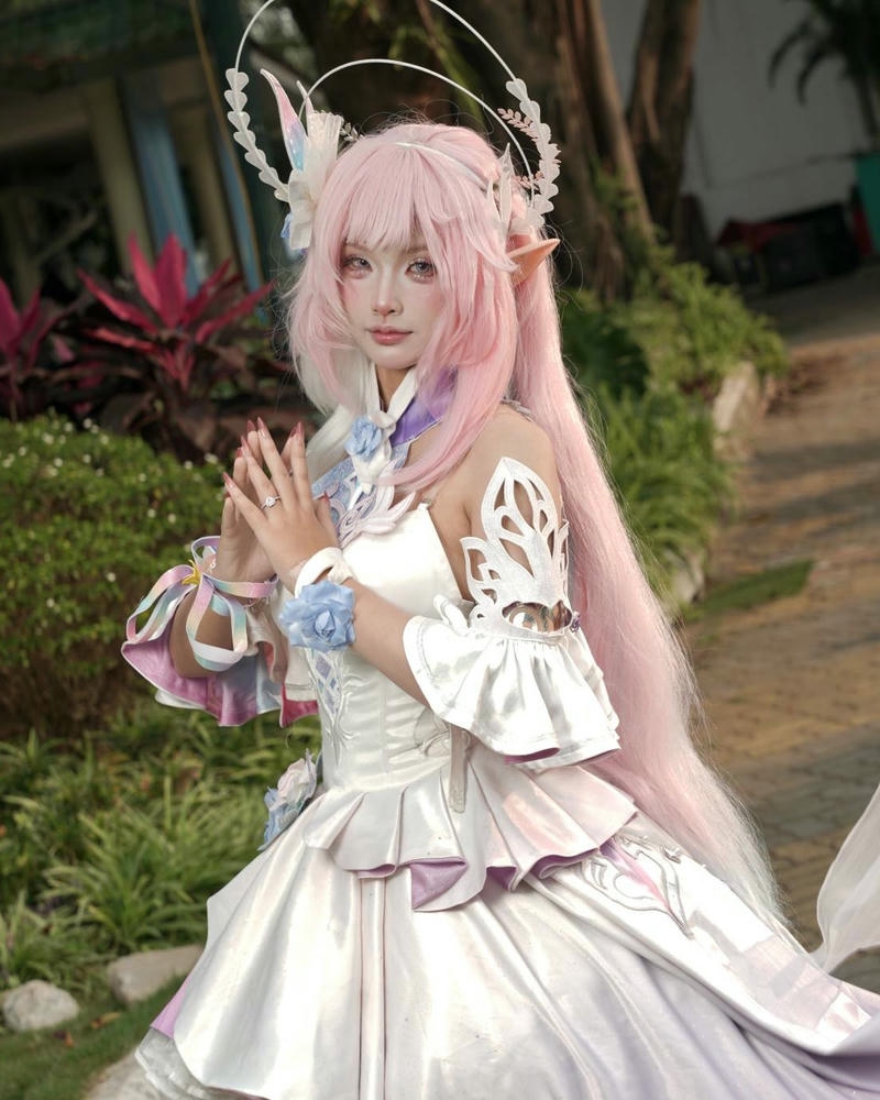 Cosplay anime nữ rồng tóc hồng váy trắng đứng trong vườn