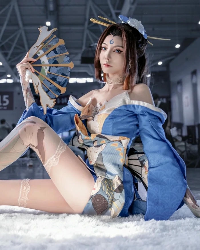Mai Shiranui cosplay mặc váy xanh ngồi trên thảm lông trắng