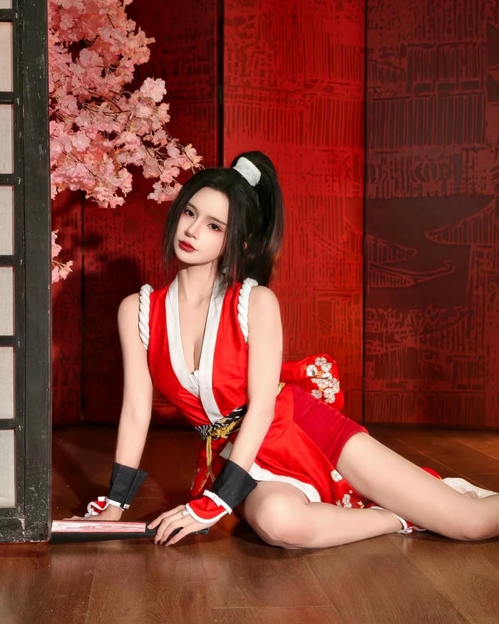 Mai Shiranui cosplay nằm nghiêng trên sàn gỗ cầm quạt giấy