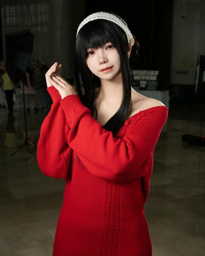 Yor Briar mặc áo len đỏ đứng cười bẽn lẽn dễ thương